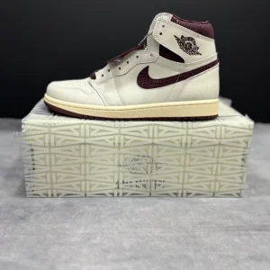 کتونی نایکی جردن 1 های آ ما مانی‌یر با جیر سفید و چرم پوست‌ماری بورگوندی در پس‌زمینه روشن