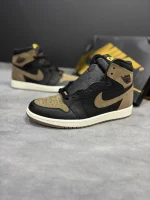 کتونی نایکی جردن 1 رترو های پالومینو با چرم مشکی و جیر قهوه‌ای در پس‌زمینه روشن