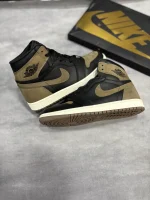 کتونی نایکی جردن 1 رترو های پالومینو با چرم مشکی و جیر قهوه‌ای در پس‌زمینه روشن