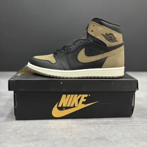 کتونی نایکی جردن 1 رترو های پالومینو با چرم مشکی و جیر قهوه‌ای در پس‌زمینه روشن