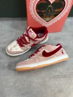 کتونی نایکی اس‌بی دانک لـو استرنج لاو با مخمل صورتی و جیر قرمز در پس‌زمینه روشن