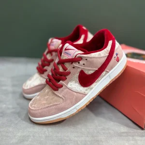 کتونی نایکی اس‌بی دانک لـو استرنج لاو با مخمل صورتی و جیر قرمز در پس‌زمینه روشن