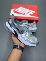 کتونی نایکی V2K Run گری/میدنایت نوی با مش خاکستری و روکش‌های آبی در پس‌زمینه روشن