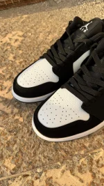 کتونی نایکی جردن 1 لو پاندا با چرم مشکی و سووشهای سفید در پسزمینه روشن