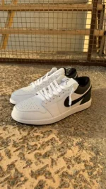 کتونی نایکی جردن 1 لو ریورس پاندا با چرم سفید و سووشهای مشکی در پسزمینه روشن