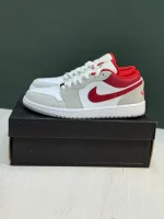 کتونی نایکی جردن 1 لو اسموک گری/رِد با چرم خاکستری و سووش‌های قرمز در پس‌زمینه روشن