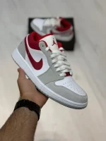 کتونی نایکی جردن 1 لو اسموک گری/رِد با چرم خاکستری و سووش‌های قرمز در پس‌زمینه روشن